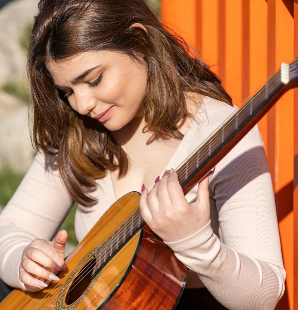 mujer joven blanca tocando la guitarra en un día soleado